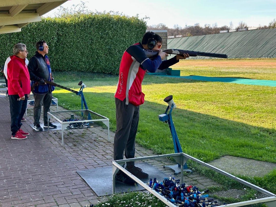Trapshooting athlete training on an Olympic trap range while Academy coaches observe from the adjacent station