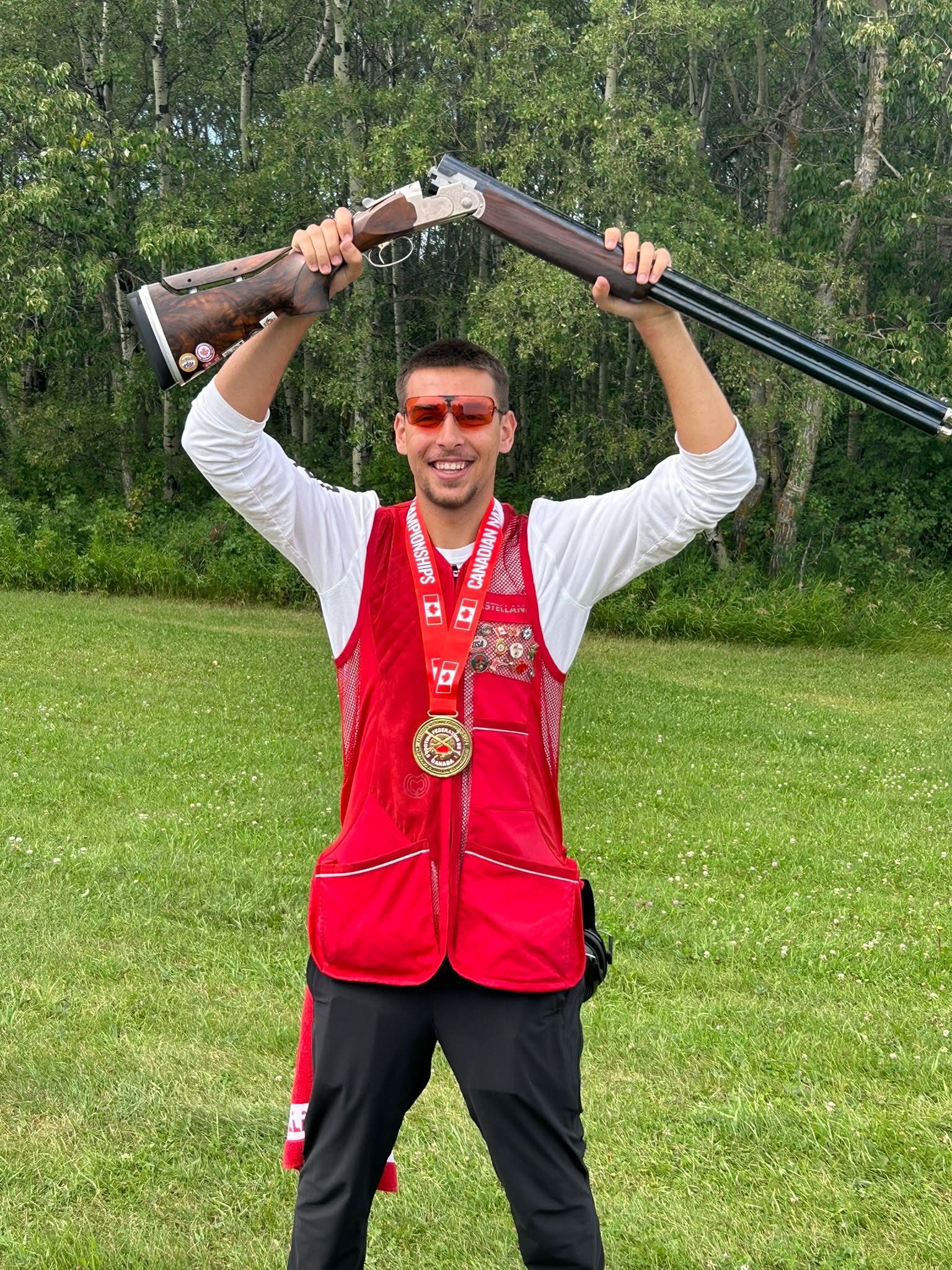 Trapshooting athlete celebrating a Canadian National Championship with a medal and shotgun raised overhead